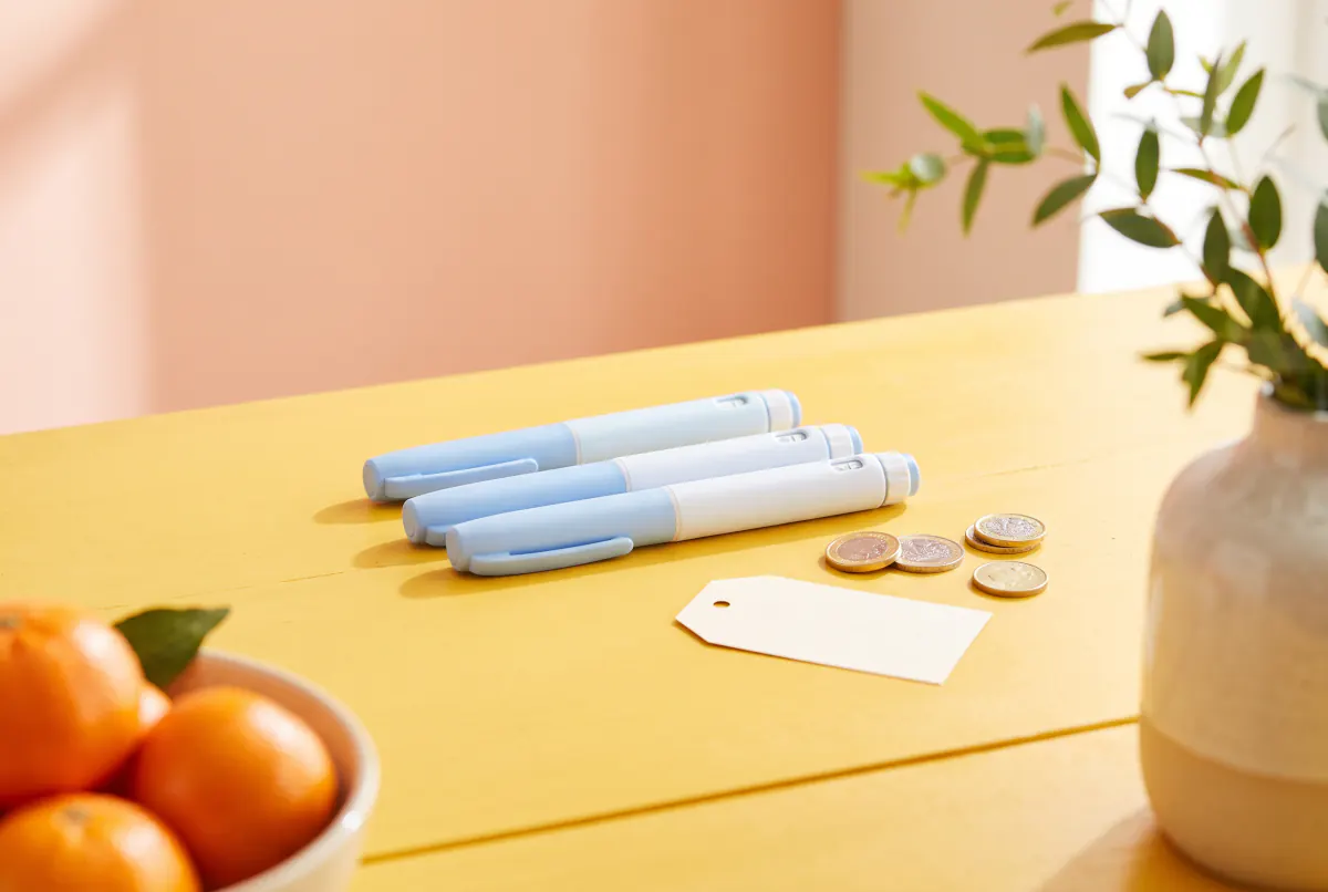 Plain sky-blue injection pens and a few coins on a sunny yellow table